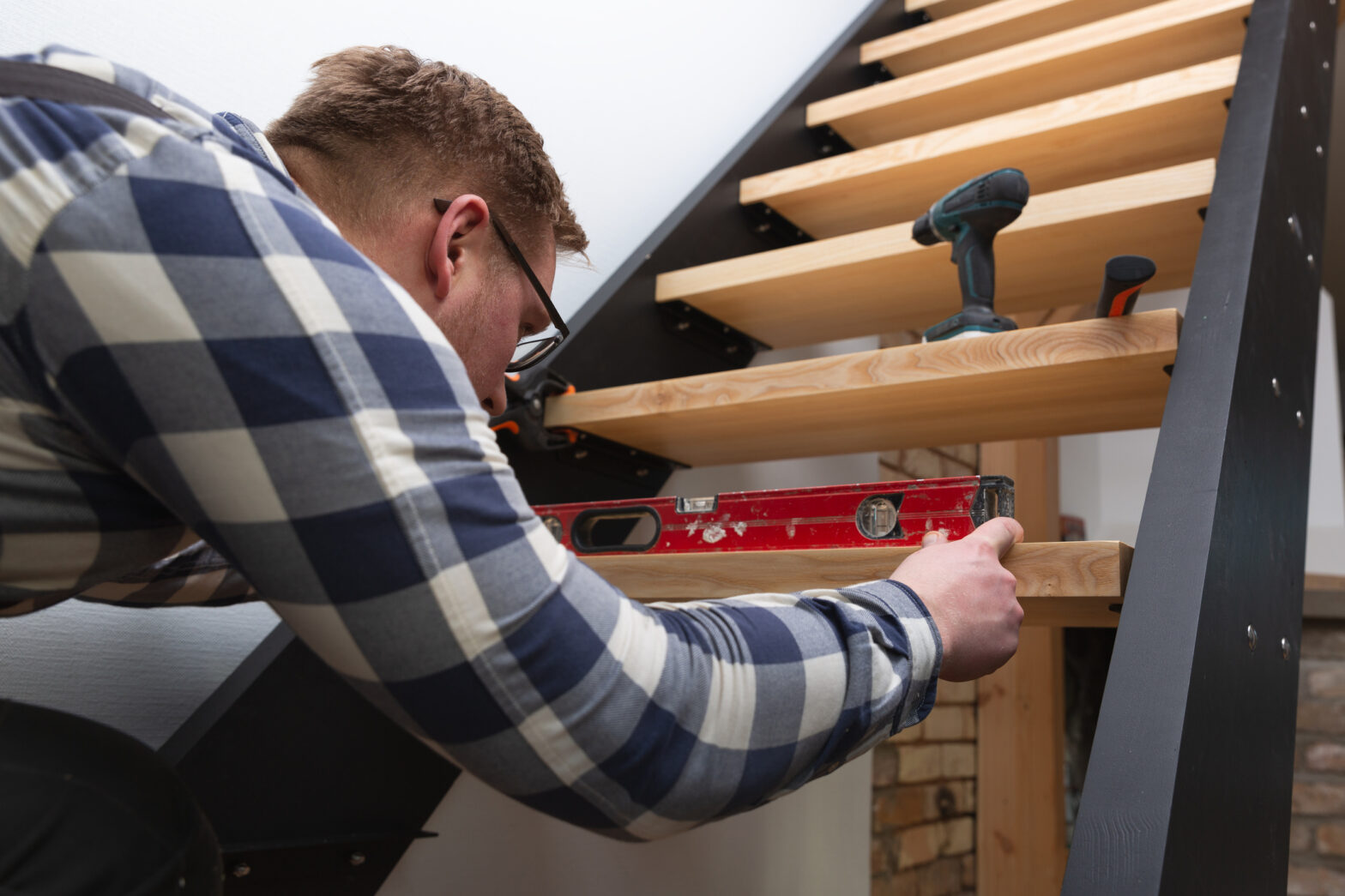 Carpenter installing a modern staircase, using a level to ensure precision. Wooden treads and black metal frame create a contemporary design.